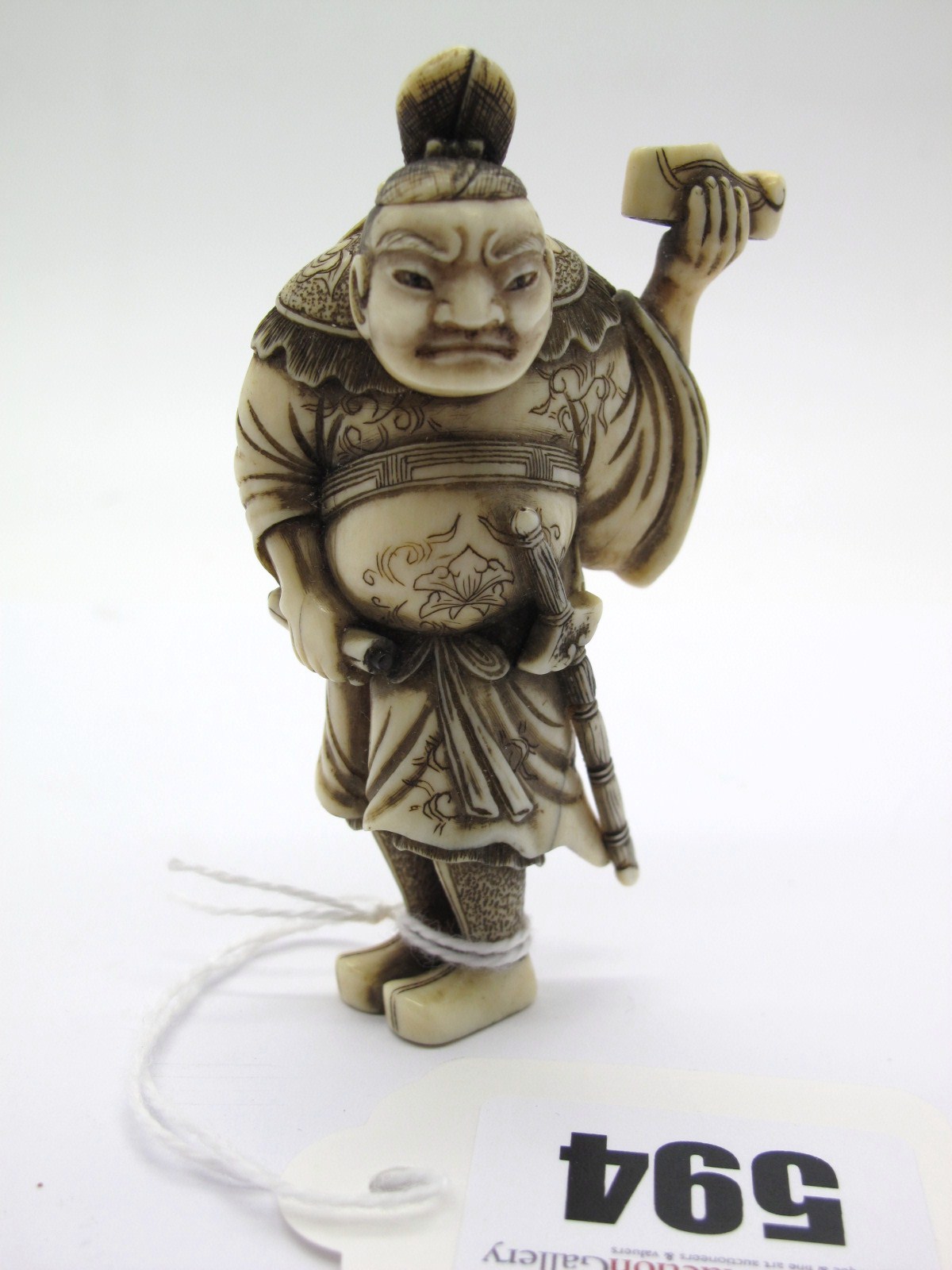 A Late XIX Century Japanese Ivory and Horn Netsuke, as a robed figure, wearing a sword, holding a