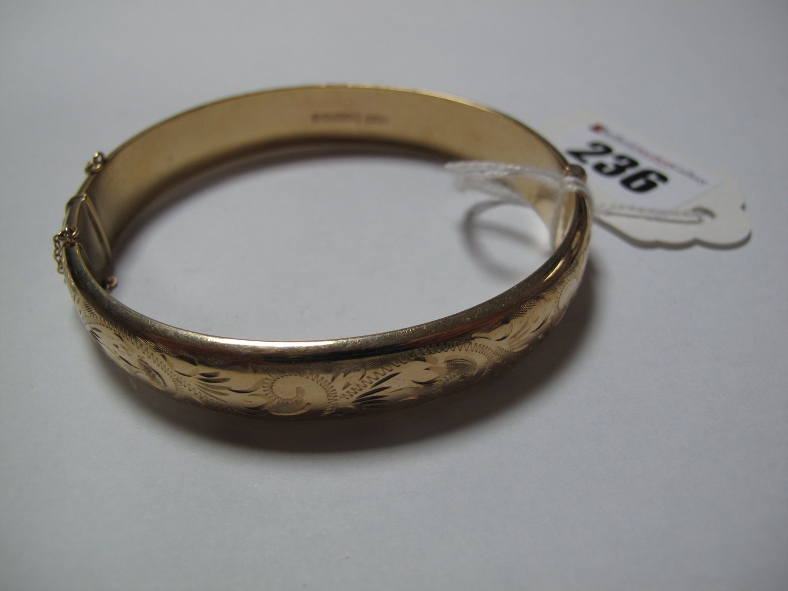 A 9ct Gold Bangle, allover leaf scroll engraved, hinged to snap clasp.