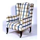 An Edwardian wing armchair, circa 1900, with checked upholstered frame and ebonised tapering legs,