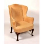 A George I style wing armchair, raised on mahogany cabriole supports,