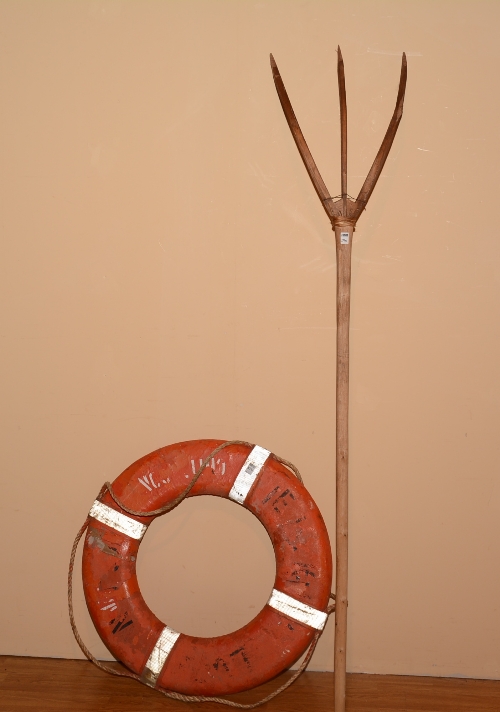 A vintage life belt, painted in orange, 74cm diameter, with a wooden three pronged pitch fork,