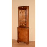 A reproduction yew wood corner cabinet, the glazed door enclosing glass shelves above panelled door,