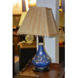 An opaque glass vase/lamp with shade, decorated with floral panels on blue ground,