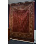 A Bokhara style machine made carpet, with multiple guls to centre over red ground, with beige,