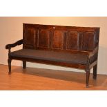 A vintage wooden panelled hall bench, with panelled back above slatted seat and scroll arm rests,