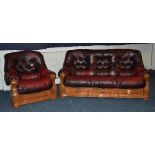 A red leather settee with matching armchair, raised on oak frame,