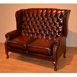 A Queen Anne style ox blood leather two seater wing back settee, with button back,