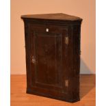 An 18th century oak wall mounting corner cabinet, with panelled door enclosing shelved interior,