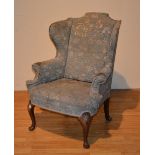 An early 20th century Queen Anne style walnut upholstered wing armchair, terminating on pad foot,