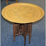 A Burmese brass top table, raised on folding carved hardwood supports, 55.5cm high x 64.