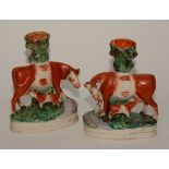A pair of Staffordshire pottery cow and calf spill vases, painted in orange and green,