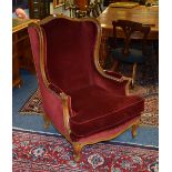 A French high back wing armchair, upholstered in red velour,
