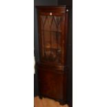 A reproduction corner cabinet, with glazed door enclosing shelved interior above panelled door,
