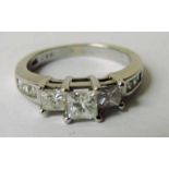 A modern white gold three stone diamond ring with three square cut stones flanked by triple stone