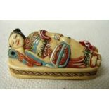 An early 20th century Japanese ivory Netsuke, a robed lady holding a fan, asleep on a bed, signed to