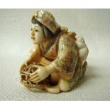 A fine Japanese ivory Netsuke, late 19th/early 20th century, a seated lady holding a basket catching