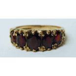 A modern 9ct gold and garnet five stone ring, the graduated stones mounted linearly in a scrolling