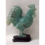 A Chinese celadon jade carved model of a standing cockerel 13cm high on a carved hardwood stand