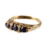 An 18ct gold and gem set ring, the traditional scroll tablet set with three dark blue stones and