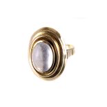 A yellow metal and moonstone ring, the oval shaped moonstone set on a higher tapering platform,