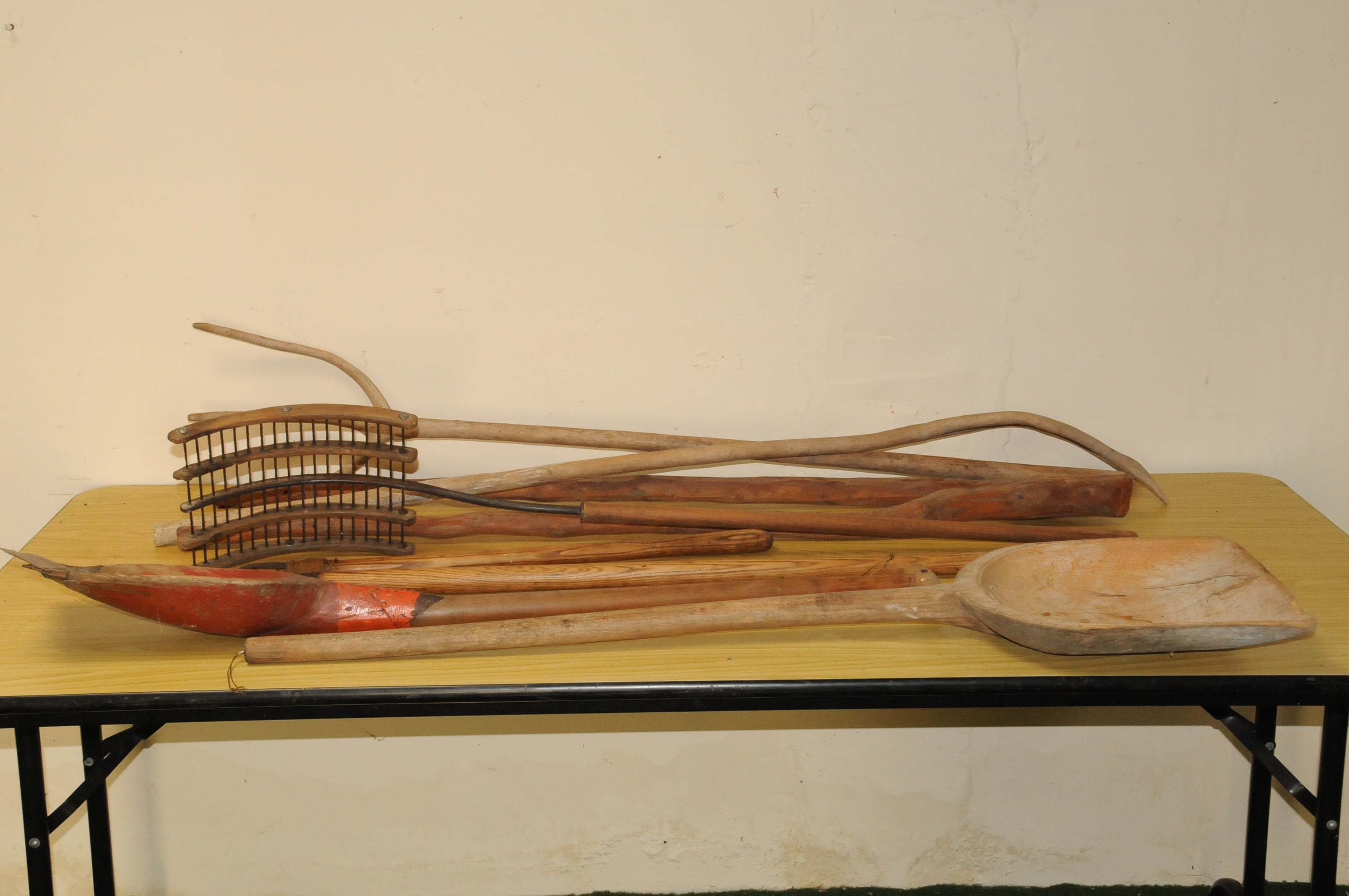 A group of antique and vintage wooden farm tools, including two pitch forks, a thrasher, two