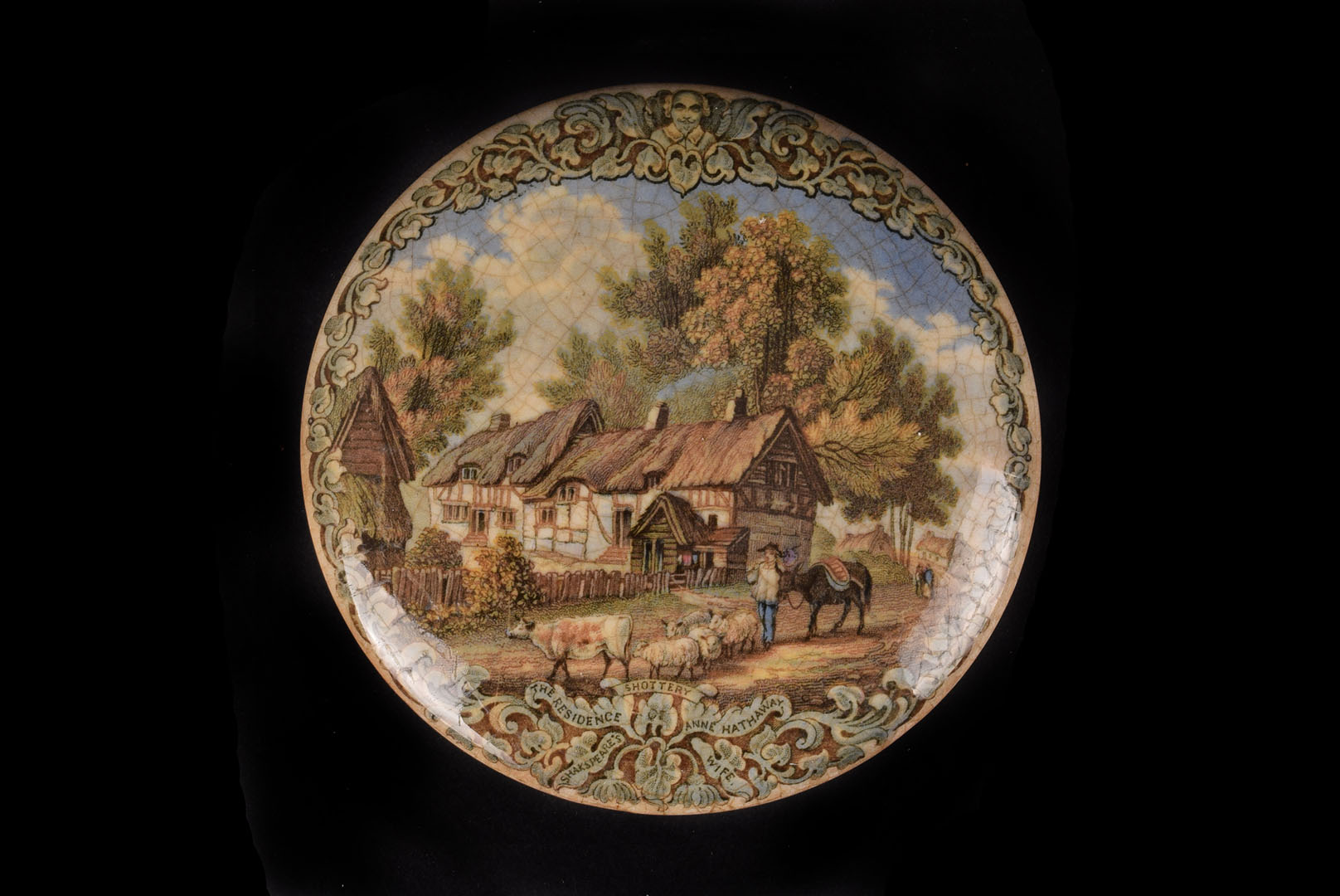 A Staffordshire pot lid, with Anne Hathaway's Cottage in oak leaf and scroll border, cracked and