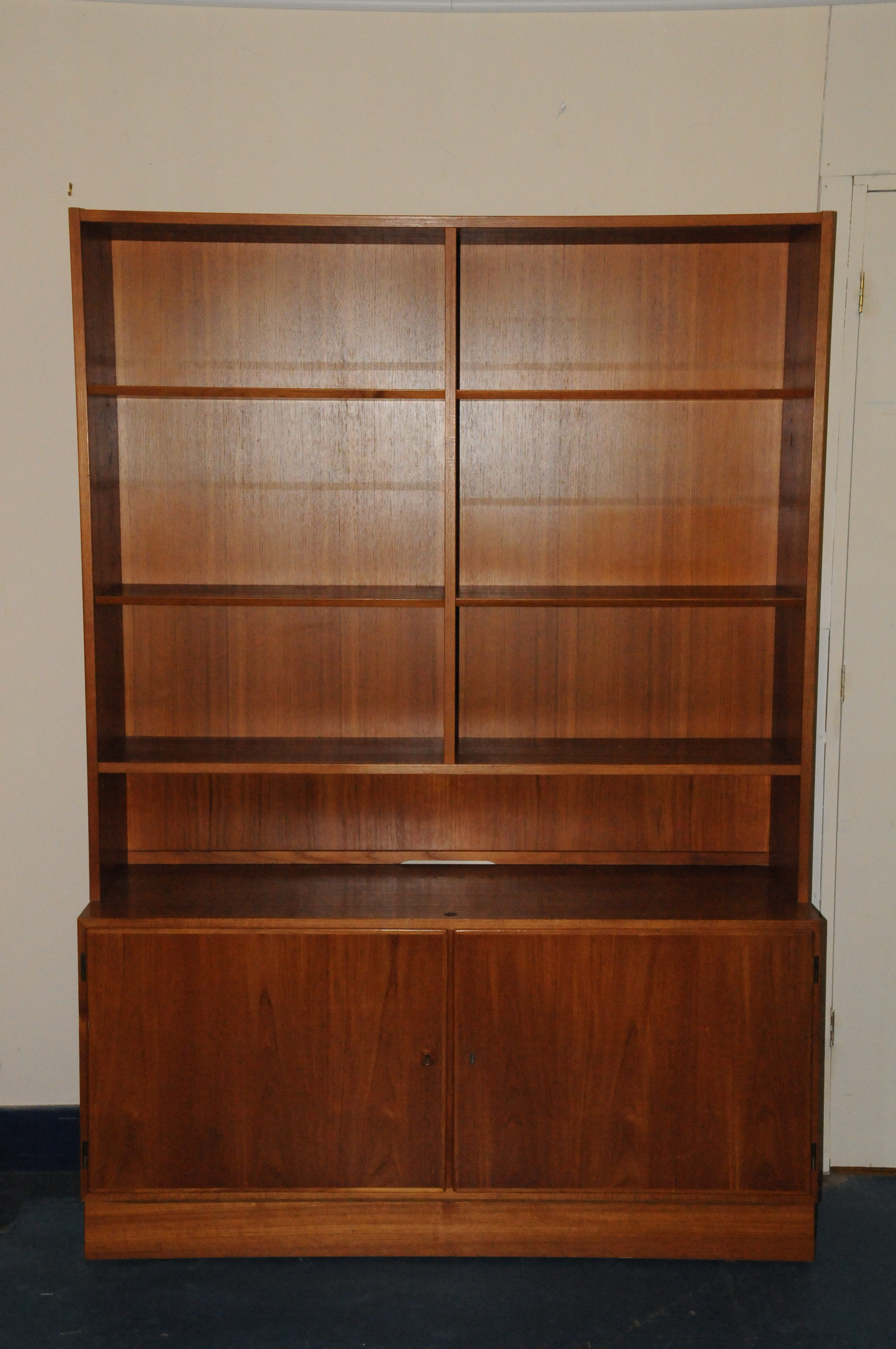 A 1970s Danish teak bookcase cabinet, the upper section with adjustable shelves, the lower with