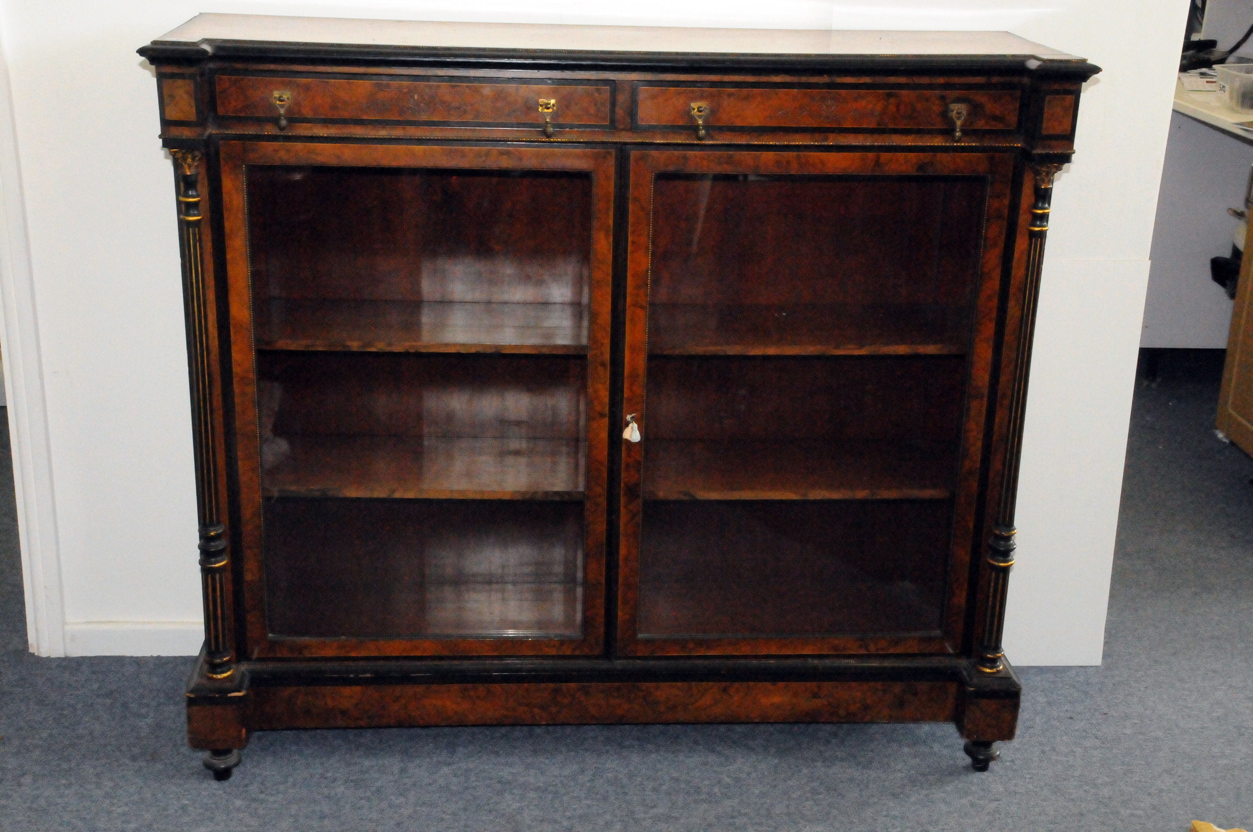 A late Victorian walnut and ebonised aesthetic glazed bookcase, having columns to each side, with