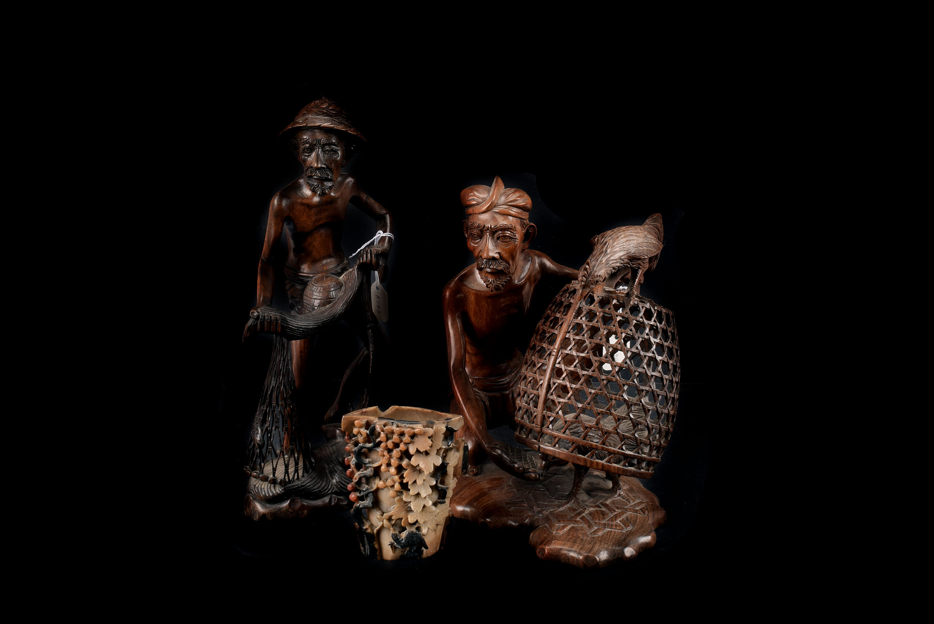 Two ornate wooden carvings, one of a fisherman with net and the other of a man feeding his chickens,