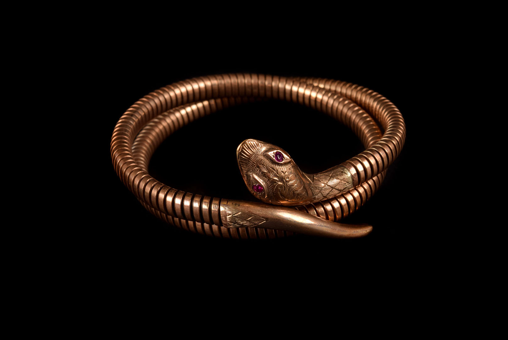 A 9ct gold snake bangle, the stretchy body leading to a decoratingly engraved head, having synthetic