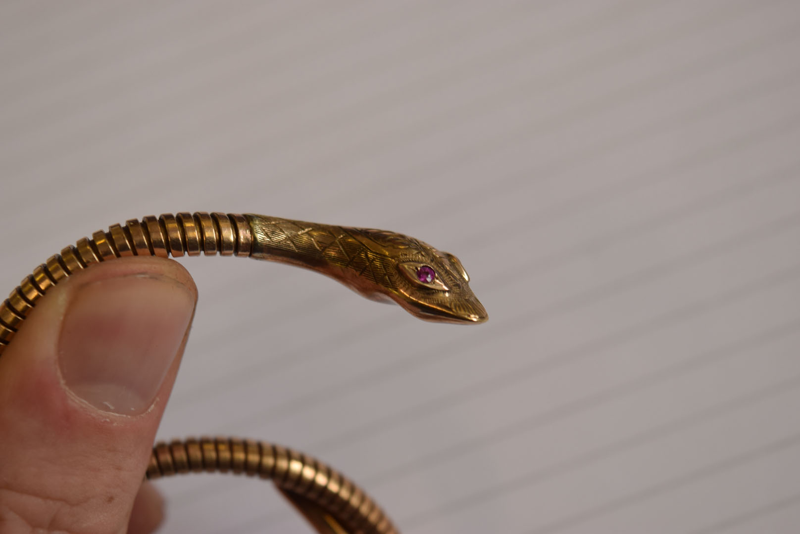 A 9ct gold snake bangle, the stretchy body leading to a decoratingly engraved head, having synthetic - Image 2 of 7