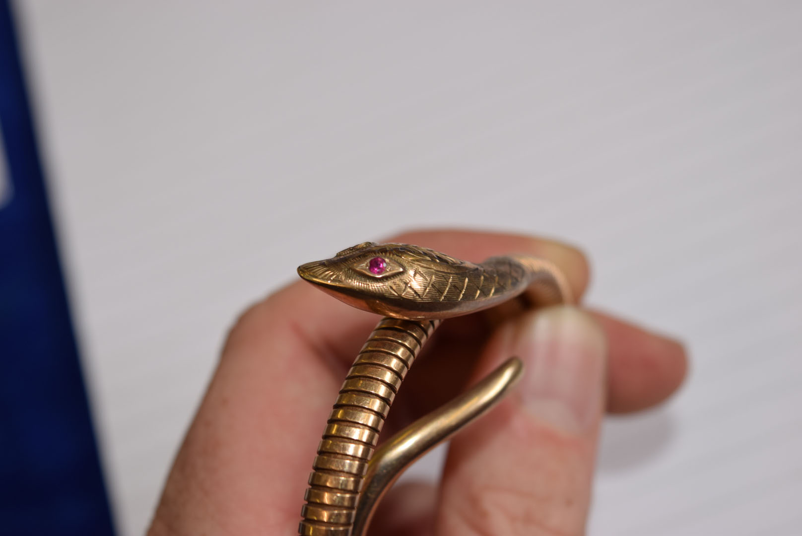 A 9ct gold snake bangle, the stretchy body leading to a decoratingly engraved head, having synthetic - Image 6 of 7