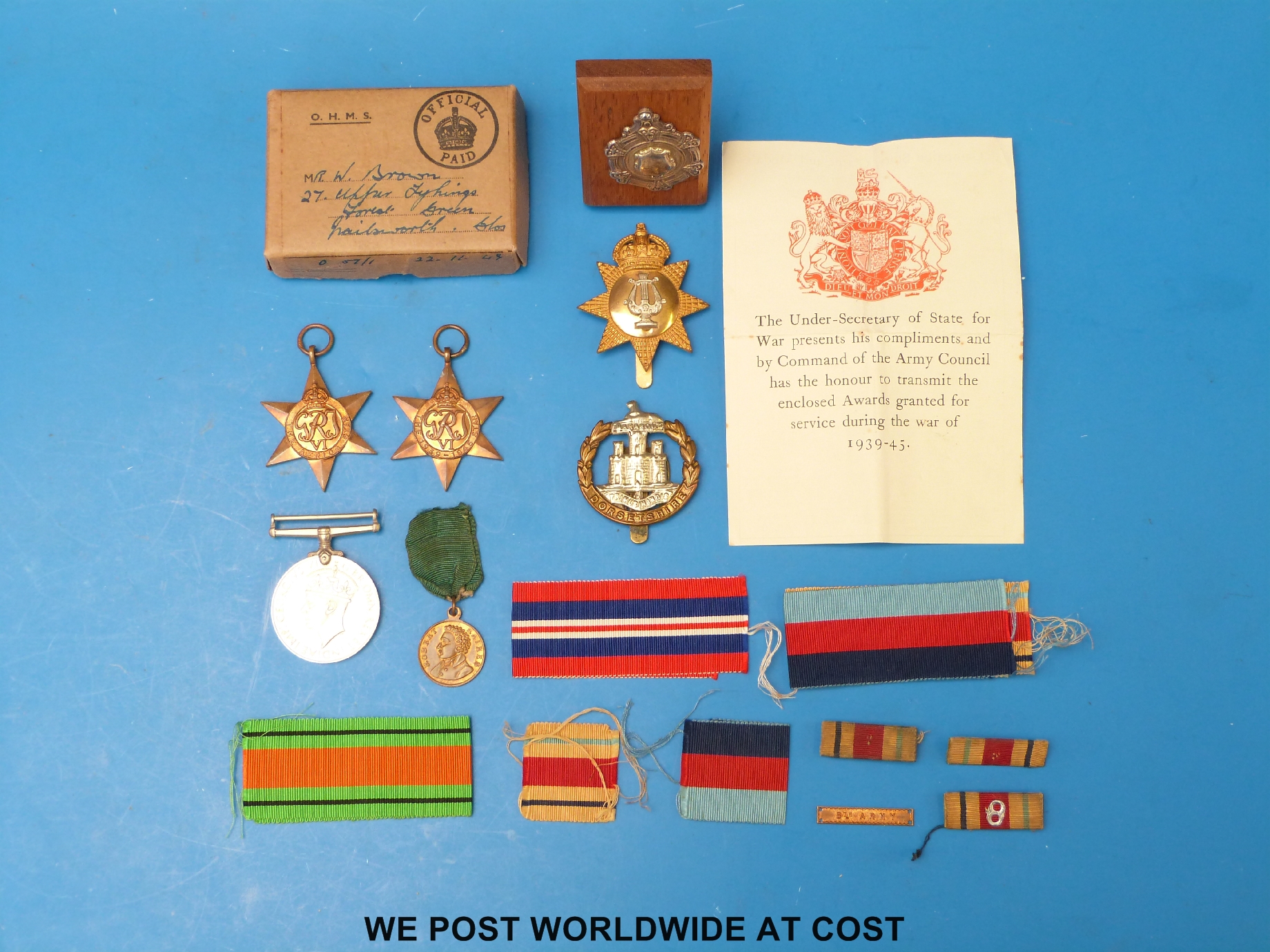 Three WWII medals, together with a Dorsetshire Regiment cap badge, and one other,