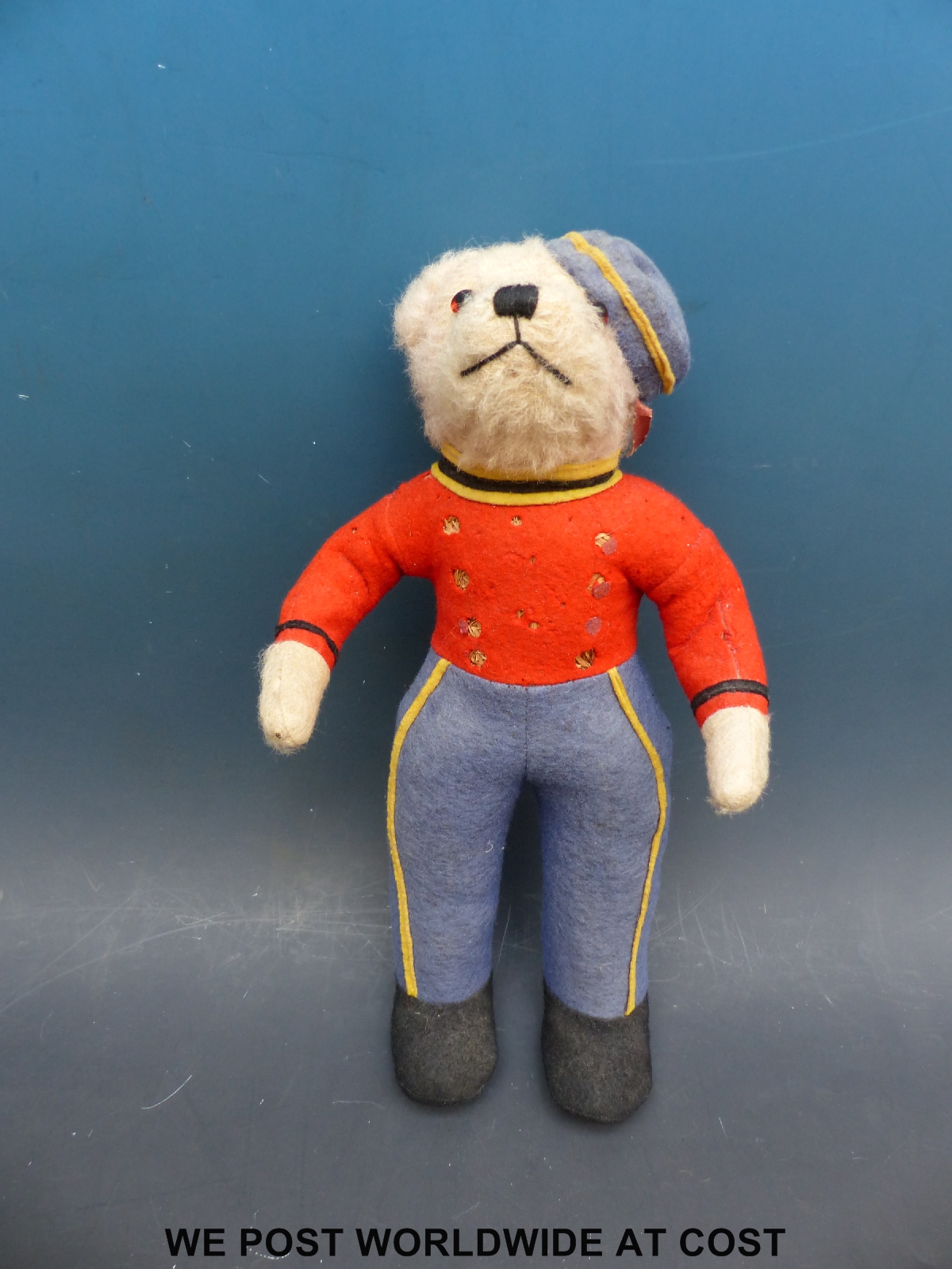 A straw filled teddy bear in red, blue and yellow railway uniform with matching hat, 35cm tall.