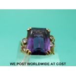 A yellow metal ring marked 14k set with a large purple sapphire with clear stones to the shoulders