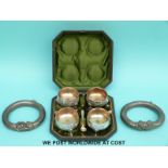 Two white metal slave bangles and a cased set of four silver plated salts