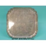 A George V hallmarked silver salver of square form raised on four feet,