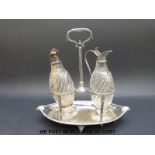 A pair of wrythen moulded cut glass condiment bottles with plated mounts in a boat shaped stand