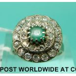 A white metal ring marked 18k set with an emerald surrounded by two rows of diamonds (size M)