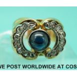 A yellow metal ring set with a sapphire cabochon and two half circles of diamonds,