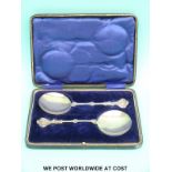 A pair of cased hallmarked silver Arts and Crafts serving spoons with decorative finials,