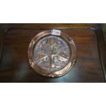A Newlyn style hammered and embossed copper dish, decorated with stylized flowers, 18.5cm diameter.