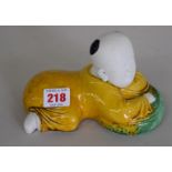 A Chinese biscuit and sancai glazed boy, laying on a cushion, 17.5cm wide.