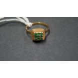 An 18k gold ring having nine small emeralds set in a rope edged square setting.