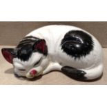 A MID 20TH CENTURY POTTERY MODEL Of a recumbent black and white cat, with a bright red nose and