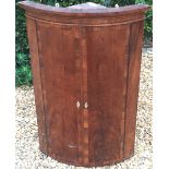 A GEORGIAN MAHOGANY AND CROSSBANDED BOW FRONTED TWO DOOR CORNER CUPBOARD.