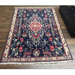 A PERSIAN WOOLLEN RUG Having a red medallion on a dark blue field, scattered with stylized floral