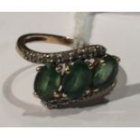A 9CT GOLD, EMERALD AND DIAMOND HALF TWIST DRESS RING The three oval cut emeralds claw set, to a