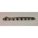 AN ART DECO PERIOD DIAMOND, EMERALD AND PASTE BAR BROOCH The graduated row of alternating old cut