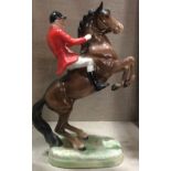 BESWICK, A POTTERY MODEL OF A HUNTSMAN Riding a rearing chestnut horse, wearing a bright red